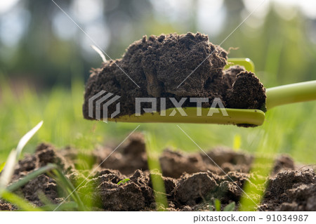 Close-up. A woman's hand loosens the ground in the garden with a garden shovel. Bright green grass and sun rays. Spring, earth care Close-up. A woman's hand loosens the ground in the garden with a garden shovel. Bright green grass and sun rays. Spring, earth care 91034987