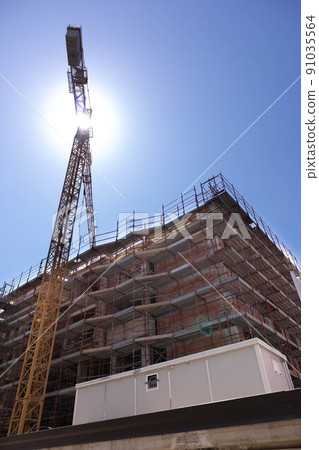 building under construction with scaffolding, yellow crane and blue sky 91035564