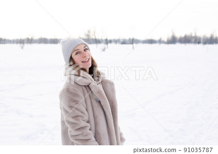 Young girl in beige clothes, fur coat made of artificial fur walks in winter 91035787