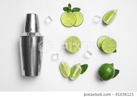 Flat lay composition with fresh juicy limes, ice cubes and cocktail shaker on white background 91036125