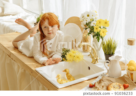 Little girl and cute ducklings are sitting in a basket in the kitchen. 91036233