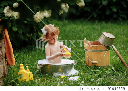 Cute little girl in a basin taking a bath in the garden. 91036259