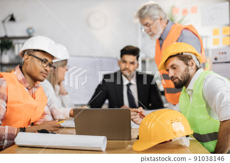 Group of coworkers in suits and helmets having business meeting at office. Group of coworkers in suits and helmets having business meeting at office. 91038146