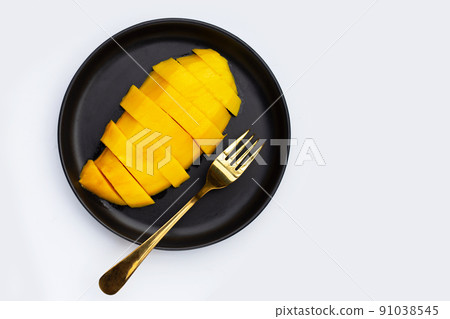 Yellow mango slices in dark plate 91038545