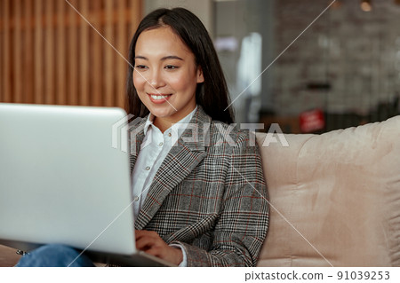 Close up of smiling asian business woman working laptop sitting in cozy office Close up of smiling asian business woman working laptop sitting in cozy office 91039253