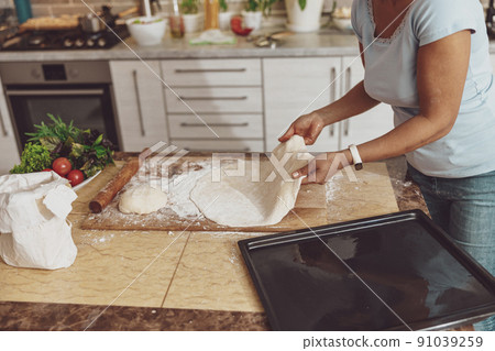 A woman in the background of the kitchen prepares dough for baking pizza in the oven A woman in the background of the kitchen prepares dough for baking pizza in the oven 91039259