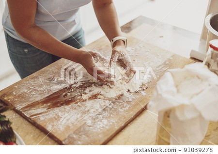Housewife kneads flour dough on a wooden board against the background of the kitchen 91039278