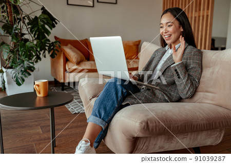 Smiling asian businesswoman making video call to client and waving greeting Smiling asian businesswoman making video call to client and waving greeting 91039287