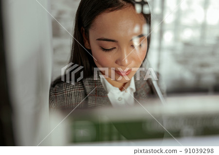 Portrait of smiling asian woman standing behind glass in office and looking down 91039298