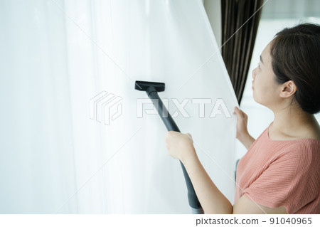 Asian young woman using vacuum machine to cleanup the dust on curtain in living room close up. Housework and chores in daily life concept. Housekeeper cleaning a white curtain. Asian young woman using vacuum machine to cleanup the dust on curtain in living room close up. Housework and chores in daily life concept. Housekeeper cleaning a white curtain. 91040965
