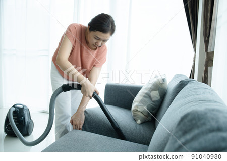 Asian young woman using vacuum machine to cleanup the dust on curtain in living room close up. Housework and chores in daily life concept. Housekeeper cleaning a white curtain. Asian young woman using vacuum machine to cleanup the dust on curtain in living room close up. Housework and chores in daily life concept. Housekeeper cleaning a white curtain. 91040980