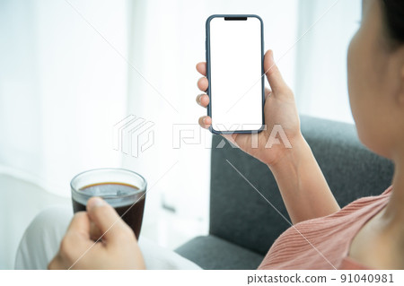 Mockup smartphone with isolated blank screen. Young Asian woman texting and exploring social media on a smartphone while drinking coffee in morning. Young woman drinking a cup of coffee in morning. 91040981