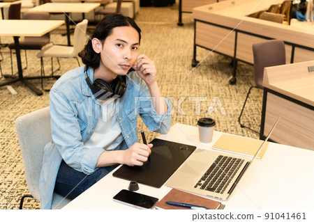 A man wearing headphones and working on a pen tablet A man wearing headphones and working on a pen tablet 91041461