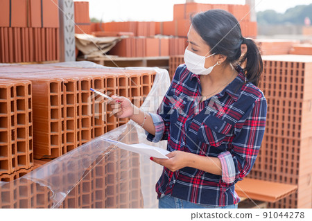 Woman in protective face mask controlling quantity of redbricks Woman in protective face mask controlling quantity of redbricks 91044278