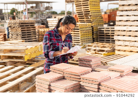 Female worker checking quantity of paving slabs in warehouse Female worker checking quantity of paving slabs in warehouse 91044292