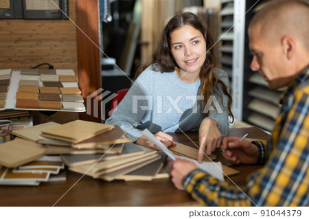 Woman seller advises a buyer in choosing a laminate in hardware store Woman seller advises a buyer in choosing a laminate in hardware store 91044379