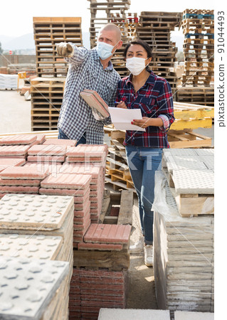 Man and woman in protective mask keep track of the number of paving slabs at the site of hardware store Man and woman in protective mask keep track of the number of paving slabs at the site of hardware store 91044493