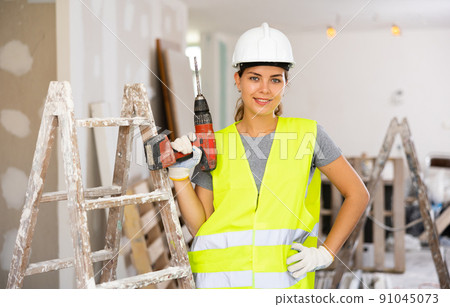 Female foreman in protective yellow vest and hard hat with screwdriver in hand Female foreman in protective yellow vest and hard hat with screwdriver in hand 91045073