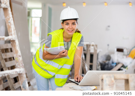 Smiling woman builder using laptop in construction site Smiling woman builder using laptop in construction site 91045145