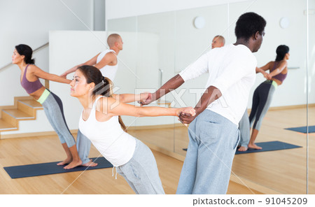 Women and men exercising assisted yoga poses in pairs 91045209