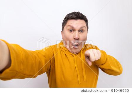 Portrait of shocked man blogger pointing at you, looking at camera with open mouth, POV, point of view of photo, wearing urban style hoodie. Indoor studio shot isolated on white background. Portrait of shocked man blogger pointing at you, looking at camera with open mouth, POV, point of view of photo, wearing urban style hoodie. Indoor studio shot isolated on white background. 91046960