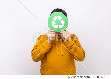 Anonymous male person hiding face behind green recycling sign, garbage sorting and environment protection, wearing urban style hoodie. Indoor studio shot isolated on white background. 91046983