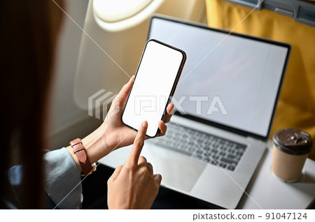Close-up image, Female traveler using a smartphone and portable laptop on the plane. 91047124