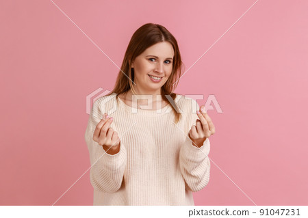 Portrait of attractive positive blond woman smiling and showing give me money gesture, asking for payment, allowance, wearing white sweater. Indoor studio shot isolated on pink background. Portrait of attractive positive blond woman smiling and showing give me money gesture, asking for payment, allowance, wearing white sweater. Indoor studio shot isolated on pink background. 91047231