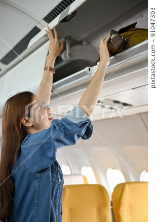 Beautiful young asian woman putting her bag at overhead locker or overhead compartment. 91047303