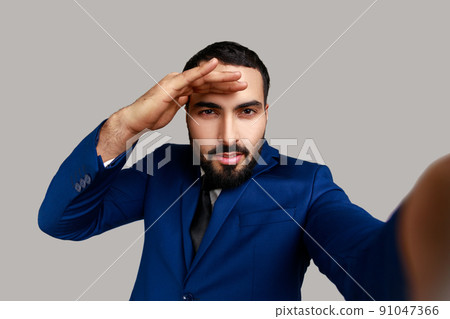 Positive handsome bearded businessman looking into distance with calm facial expression, point of view, wearing official style suit. Indoor studio shot isolated on gray background. Positive handsome bearded businessman looking into distance with calm facial expression, point of view, wearing official style suit. Indoor studio shot isolated on gray background. 91047366
