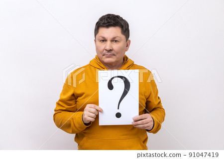 Good looking middle aged man holding question mark, finding smart solution, asking for advice, looking at camera, wearing urban style hoodie. Indoor studio shot isolated on white background. Good looking middle aged man holding question mark, finding smart solution, asking for advice, looking at camera, wearing urban style hoodie. Indoor studio shot isolated on white background. 91047419