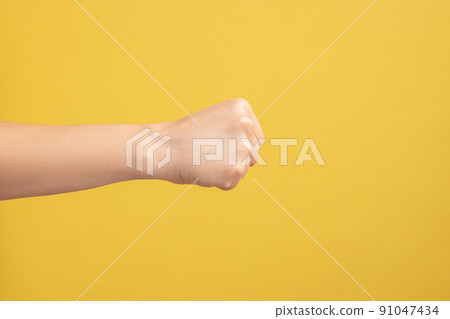 Profile side view closeup of woman hand showing boxing fists with hand, attack or defense against problems. Indoor studio shot isolated on yellow background. Profile side view closeup of woman hand showing boxing fists with hand, attack or defense against problems. Indoor studio shot isolated on yellow background. 91047434