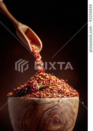 Chilli flakes are poured into a wooden dish. Chilli flakes are poured into a wooden dish. 91050849