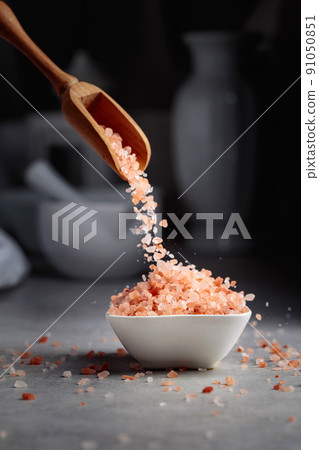 Pink salt in crystals is poured into a small white bowl. 91050851