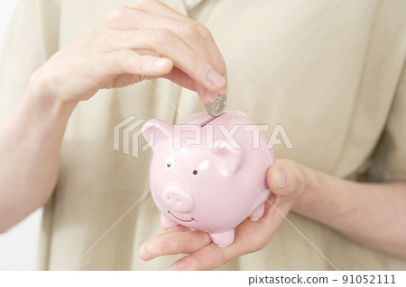 Close-up of a middle-aged woman who puts coins in a piggy bank Close-up of a middle-aged woman who puts coins in a piggy bank 91052111