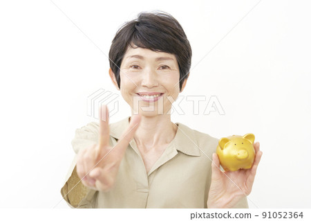 A middle-aged woman holding a piggy bank and signing a peace sign on a white background A middle-aged woman holding a piggy bank and signing a peace sign on a white background 91052364