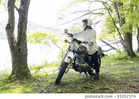 A young woman riding a motorcycle by the lake, a motorcycle girl 91052374