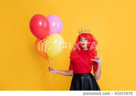surprised child in crown with party balloon on yellow background 91053070