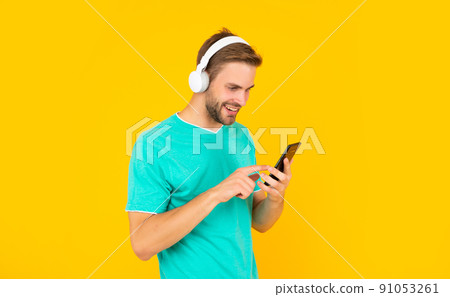Happy young man texting message on mobile phone listening to digital music in headphones, sms 91053261