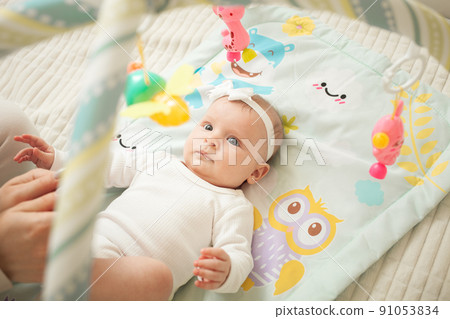 child lies on bed, hanging toys, baby mat, newborn girl. developing, watching toys, satisfied. cute and funny child lies on bed, hanging toys, baby mat, newborn girl. developing, watching toys, satisfied. cute and funny 91053834