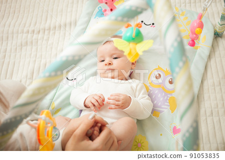 child lies on bed, hanging toys, baby mat, newborn girl. developing, watching toys satisfied 91053835