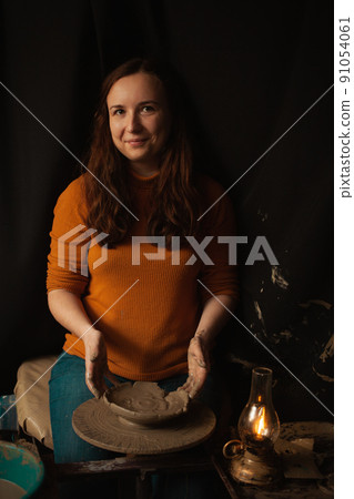 woman makes plate of clay in pottery workshop, smiles, happy, beautiful, background, authentic atmosphere, lifestyle. yellow lamp. looks into camera 91054061