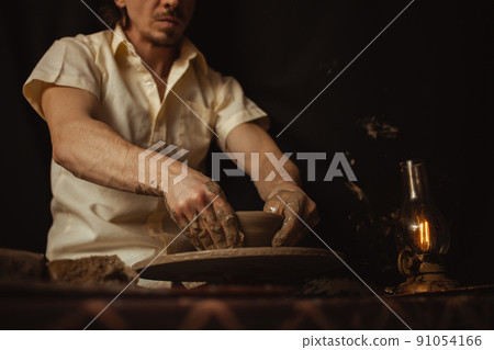 man in pottery workshop makes plate of clay, an authentic atmosphere, yellow lamp, lifestyle, magical atmosphere. Concept with your own hands, home entertainment. potter's wheel 91054166
