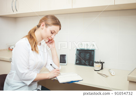 beautiful woman dentist in office, in clinic, indoor. Portrait, smiling and happy. Friendly doctor. writes in notebook beautiful woman dentist in office, in clinic, indoor. Portrait, smiling and happy. Friendly doctor. writes in notebook 91054732