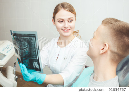 dentist shows client an X-ray of teeth of jaw, woman doctor in medical office, private clinic. smiling, happy and satisfied. dentist shows client an X-ray of teeth of jaw, woman doctor in medical office, private clinic. smiling, happy and satisfied. 91054767