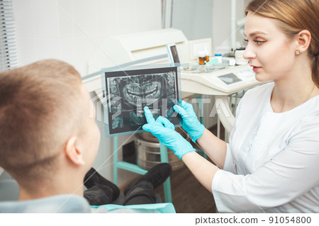 woman doctor shows patient his x-ray of teeth and explains problems. Gloves 91054800