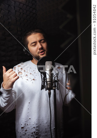 man sings into microphone, professional recording studio, headphones. Black soft walls, sound insulation. singer records his song. cute guy 91054842