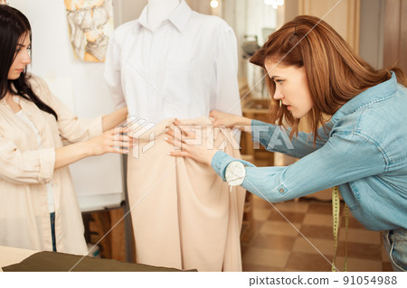 Women seamstresses apply fabric to model, mannequin. Take measurements, sewing studio in room. Creation of future clothes. Look Women seamstresses apply fabric to model, mannequin. Take measurements, sewing studio in room. Creation of future clothes. Look 91054988