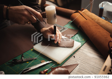 leatherworker beats with hammer. Tanner works with leather, small business, production. 91055982