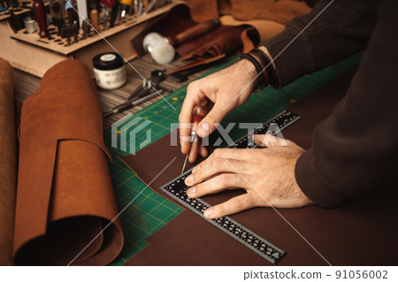leatherworker draws, measures with ruler. Tanner works with leather, small business, production. leatherworker draws, measures with ruler. Tanner works with leather, small business, production. 91056002